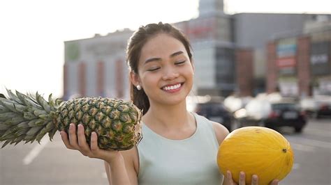 Adorable Cheerful Asian Woman Showing Melon And Peanapple In Her Hands