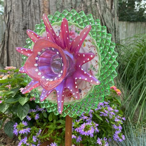 A Colorful Glass Flower Sitting On Top Of A Wooden Stick In Front Of