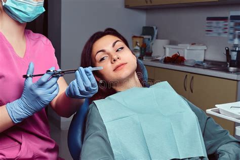 Woman Patient Sitting In A Dentist Chair While Her Doctor Preparing For Syringe Injection Stock