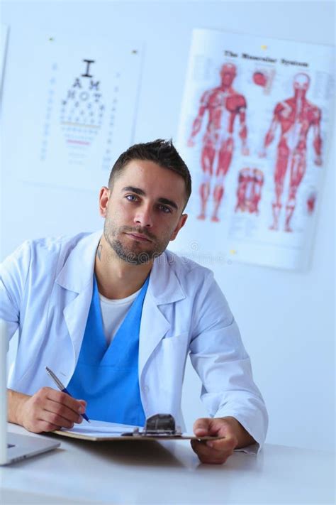 Portrait Of A Male Doctor With Laptop Sitting At Desk In Medical Office