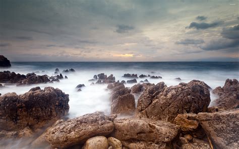 Rocks Rising From The Misty Ocean Water Towards The Sunset Wallpaper