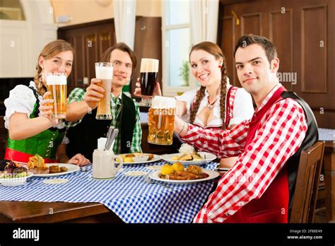 Young People In Traditional Bavarian Tracht Eating In Restaurant Or Pub