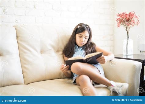 Portrait Of 9 Years Old Girl Reading A Book Sitting On Couch At Stock