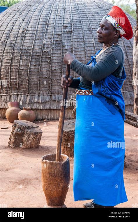 Zulu Woman In Traditional Clothing Demonstrating A Wooden Mortar And