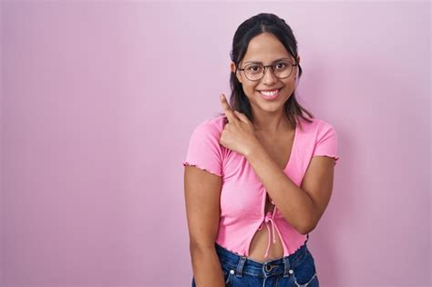 Латиноамериканская молодая женщина стоящая на розовом фоне в очках веселая с улыбкой на лице