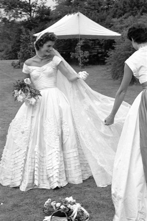 Two Women Dressed In Wedding Gowns Holding Hands And Walking Away From