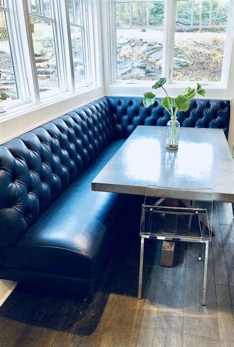 A Blue Leather Couch Sitting Under A Window Next To A Table With A Vase