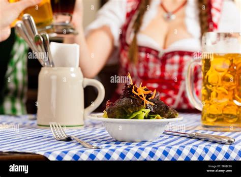 Young People In Traditional Bavarian Tracht Eating In Restaurant Or Pub