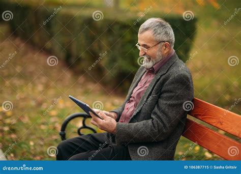 Grandpa Use A Tablet Sitting In The Park On The Bench Stock Image