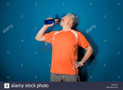 Athletic Mature Man Drinking Water From Sports Bottle Isolated On Blue