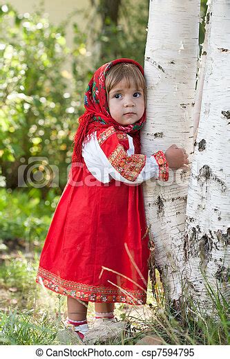 Little Girl In Russian Traditional Dress Standing Next To A Birch