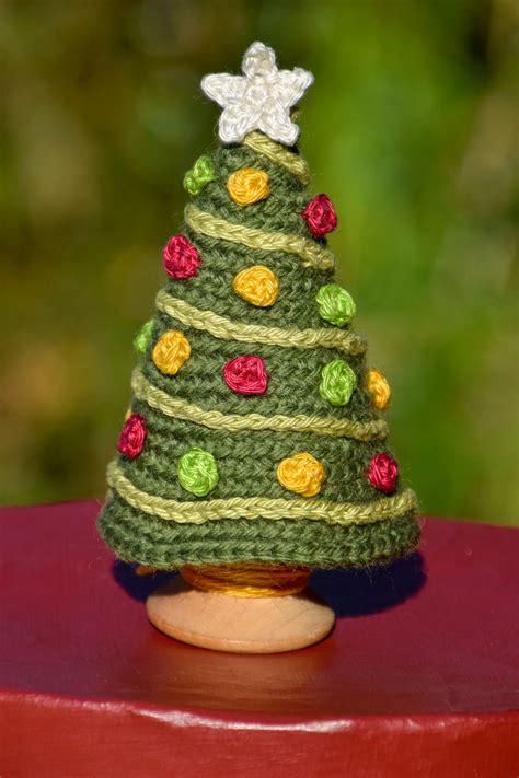 a small crocheted christmas tree sitting on top of a wooden table next to a green bush