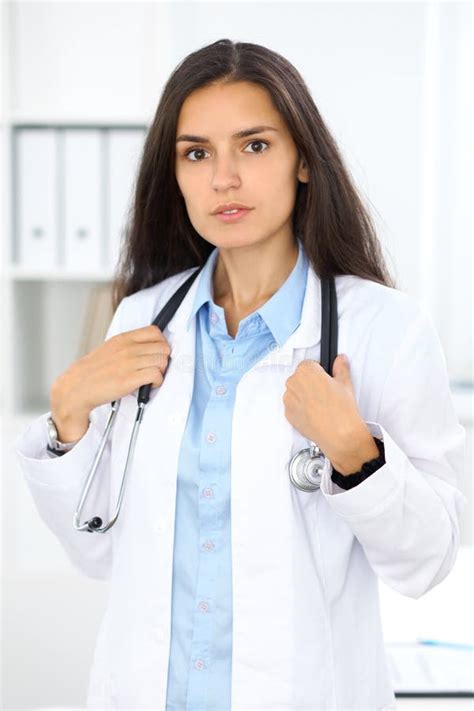 Young Brunette Female Doctor Standing And Smiling At Hospital Stock