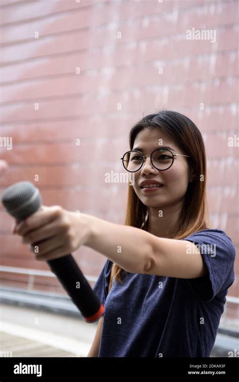 Female Journalist With Microphone Standing Against Building Stock Photo