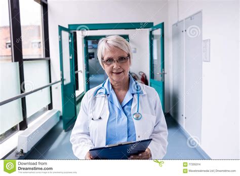 Confident Female Doctor With Clipboard Standing In Hospital Corridor