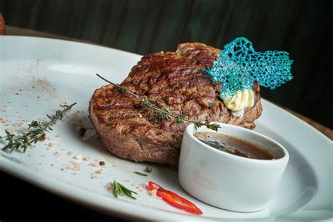 Juicy And Mouth Watering Grilled Ribeye Steak With Spicy Butter On A Black Tray With A Side Dish