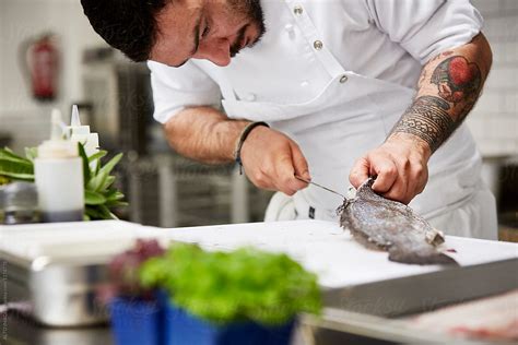 Male Chef Cutting Fish With Knife In Kitchen By Stocksy Contributor