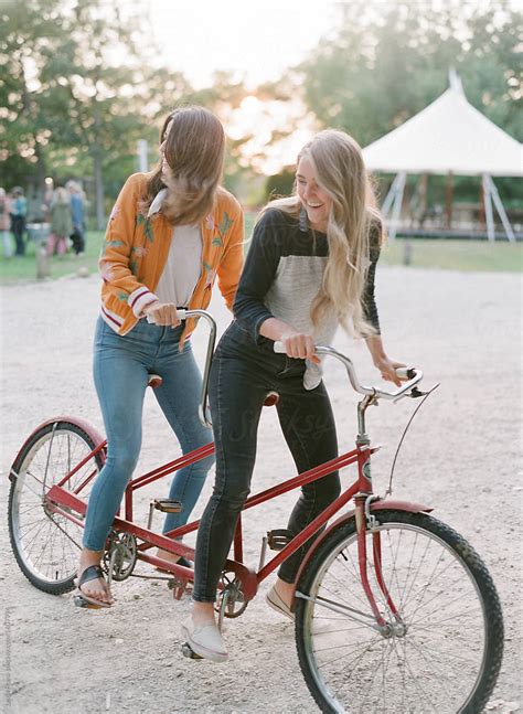 Two Millennial Women Ride A Red Tandem Bike By Stocksy Contributor