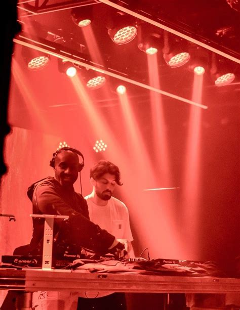 two djs in front of bright red lights at a music event with headphones on