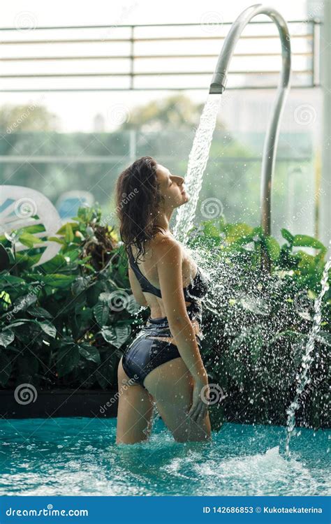 Slim Female In Swimsuit Takes Shower In Swimming Pool Between Green Bushes On Rooftop With City