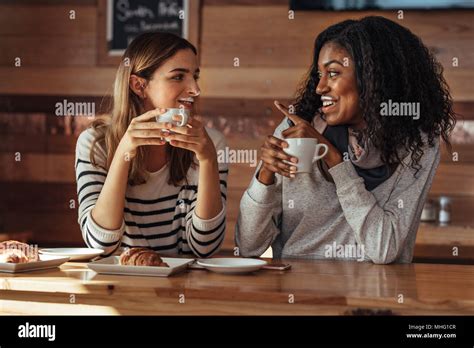 Two Women Drinking Coffee And Smiling At Each Other Pointing Towards