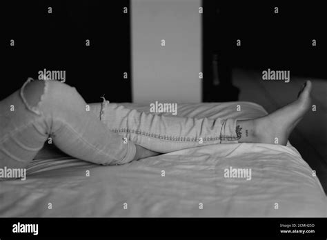 Grayscale Shot Of A Female Lying On A Bed Wearing Ripped Jeans Stock