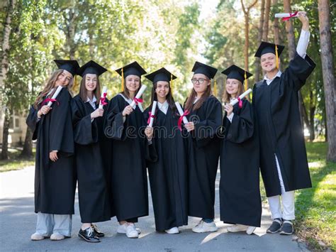 Row Of Young Students In Graduation Gowns Outdoors Showing Off Their