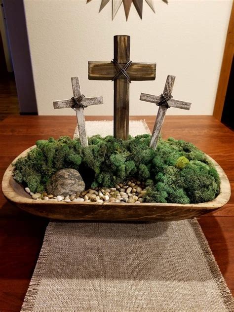 A Wooden Bowl Filled With Moss And Crosses On Top Of A Table Next To A Rug