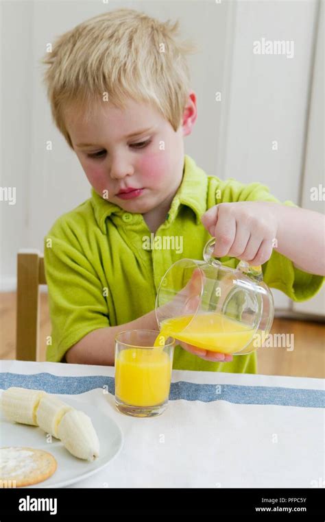 Boy Pouring Orange Juice From Jug Into Glass Stock Photo Alamy