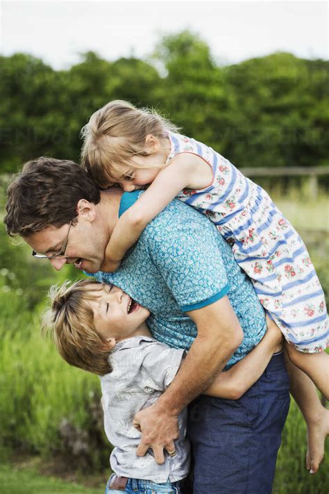 A Father And Two Children In A Garden A Boy Hugging Him Around The