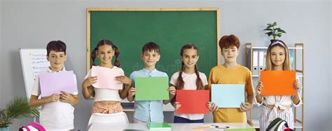 Group Of Happy School Children Standing In Classroom And Holding Paper