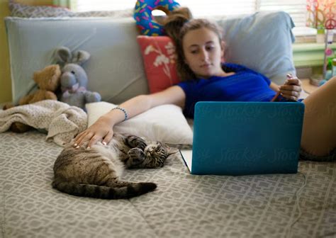 Teenage Girl On Her Laptop With Her Siamese Cat Next To Her On The Bed