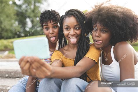 Young Women Sticking Out Tongue While Taking Selfie Through Mobile Phone At Park — Female Afro
