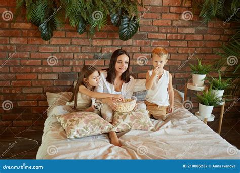 Mom Sits On The Bed With Her Son And Babe And Watch A Movie A Woman A Babe And A Girl Eat