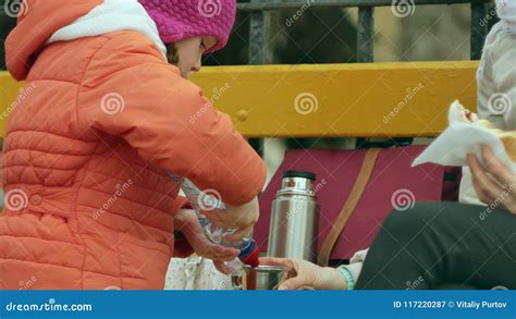 A Beautiful Girl And Her Mom Are Sitting On A Park Bench And Eating A