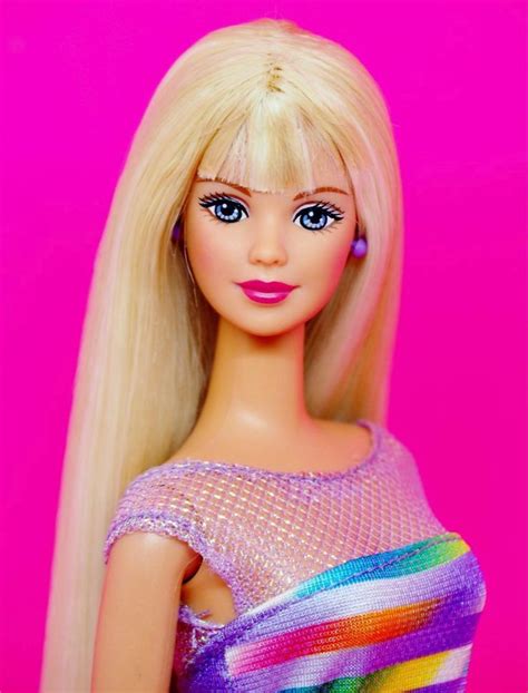 a barbie doll with long blonde hair and blue eyes wearing a colorful dress in front of a pink