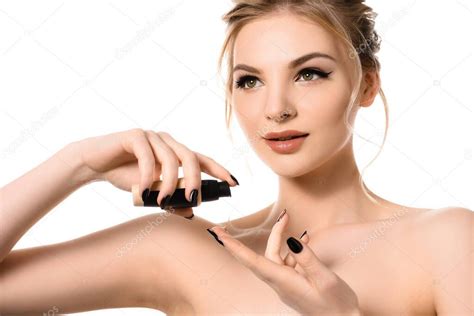 mujer rubia hermosa desnuda con maquillaje y uñas negras aplicando la base de la cara en los