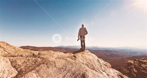 Man With A Camera On Top Of A Cliff Overlooking The Mountains Royalty