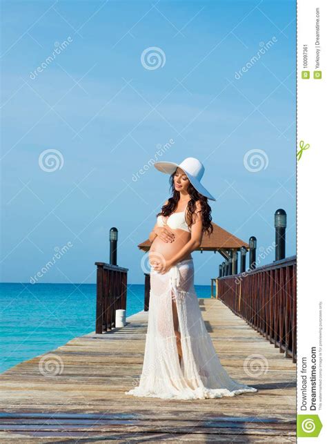 Pregnant Woman Is Standing On A Wooden Pier Hugging Her Stomach Against The Sea Dominican