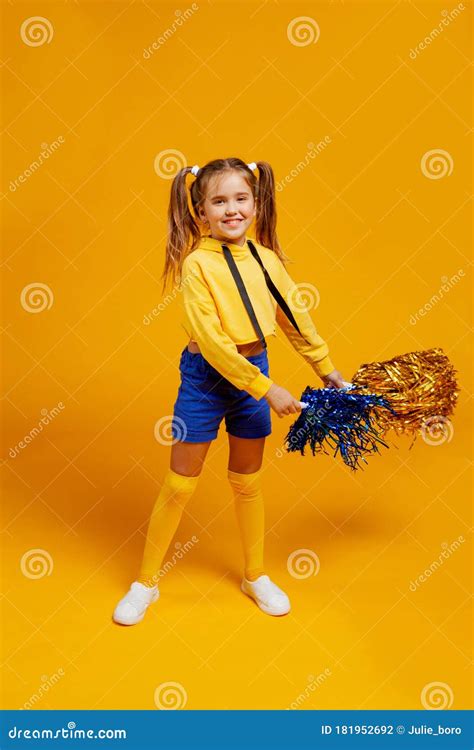 cute cheerleader girl in a yellow tank top and blue shorts is dancing with pompons in her hands