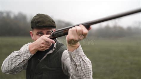 Hunter Man In Traditional Shooting Clothes On Field Aiming With Shotgun