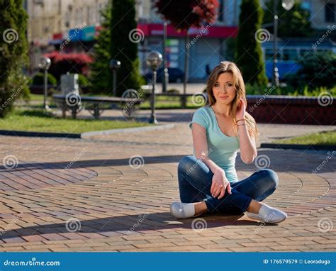 A Young And Pretty Girl In Jeans Sits On A Sidewalk Stock Image