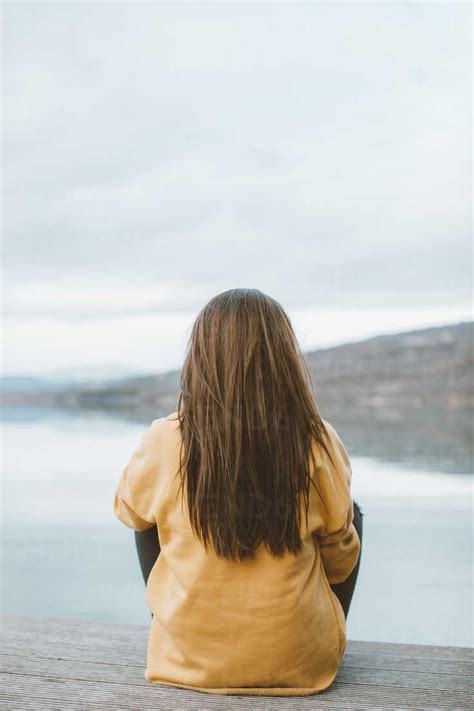 Back View Of Young Woman Sitting On Jetty Stock Photo