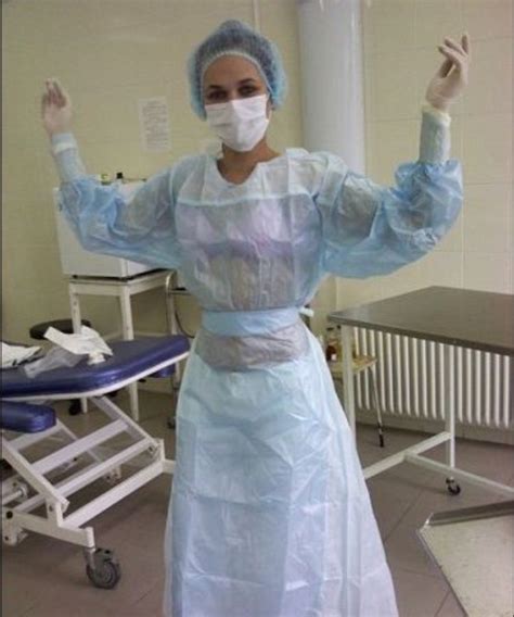 A Woman In A Hospital Gown And Face Mask Is Standing With Her Hands Up