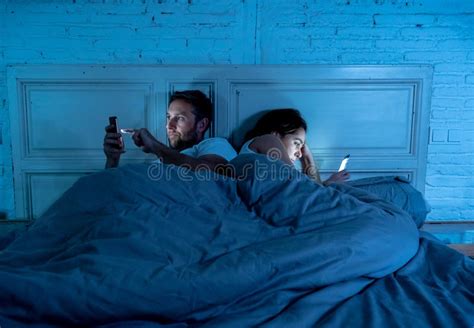 Sad And Bored Couple Addicted To Smart Mobile Phones Late At Night In Phase Of Mutual
