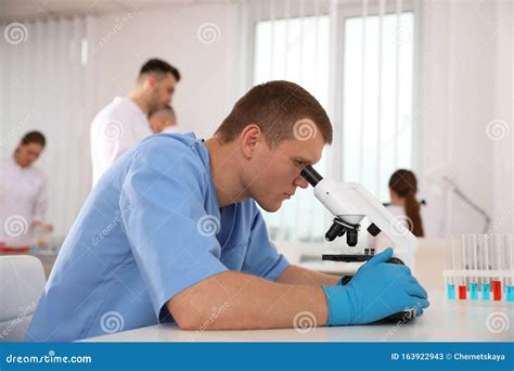 Scientist Using Microscope At Table And Colleagues Medical Research