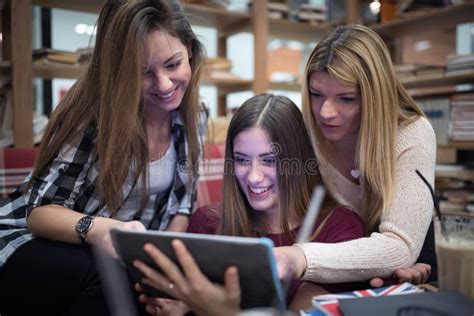 Group Of Smiling Female Students Looking At Tablet In Library Stock