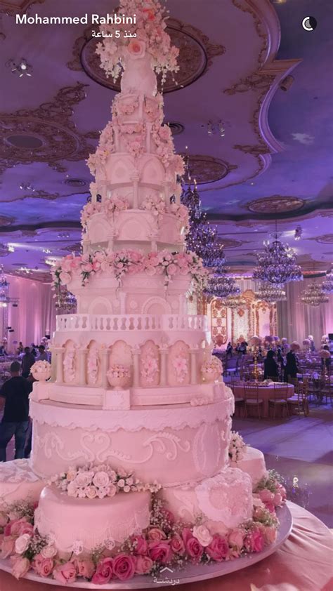 A Large Wedding Cake Sitting On Top Of A Table In A Room With Chandeliers
