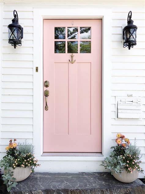 Two Planters With Flowers In Front Of A Pink Door On A White House