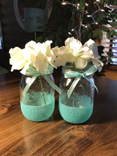 Two Mason Jars With Flowers In Them Sitting On A Table